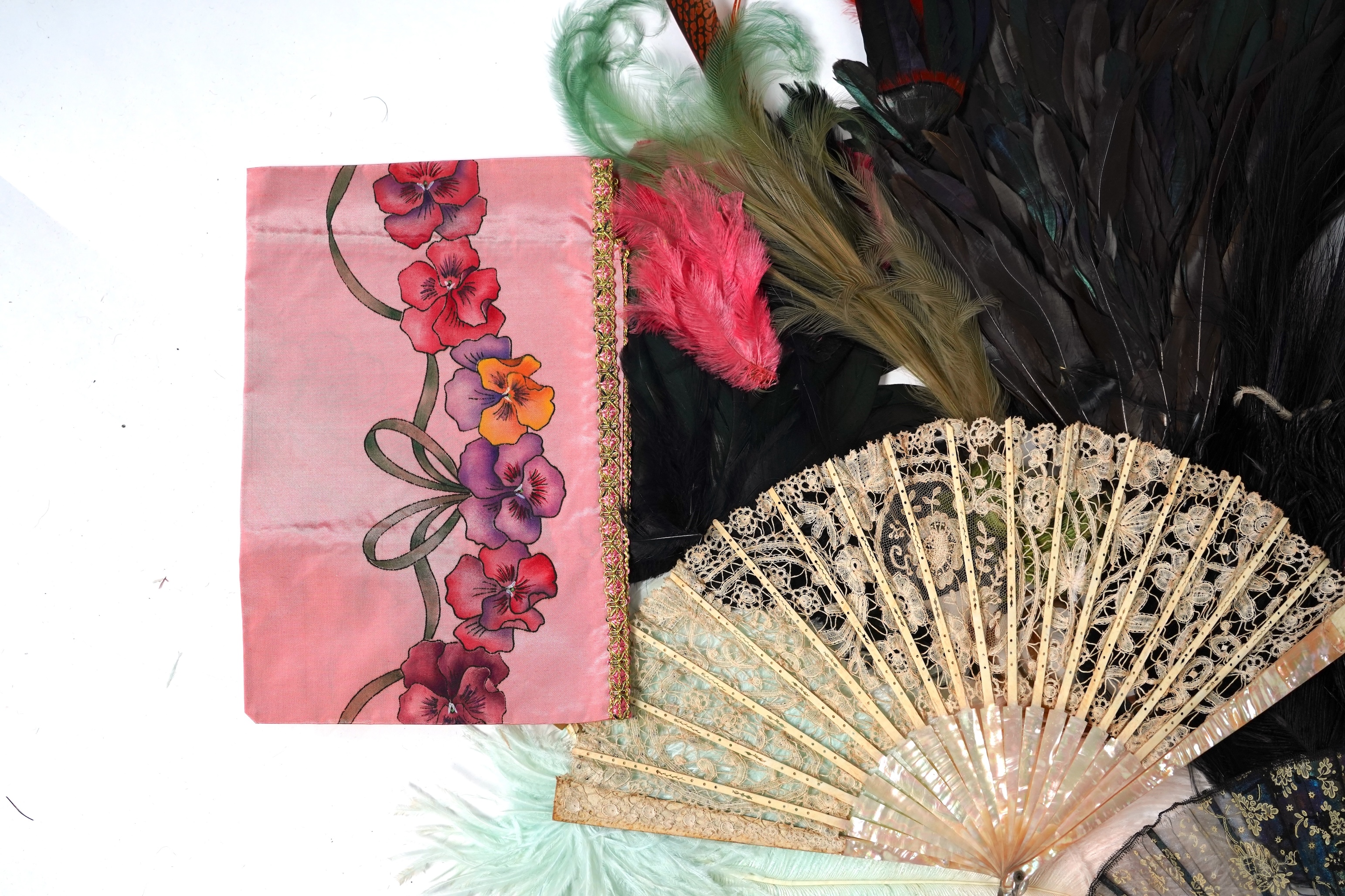 A collection of Edwardian exotic feather hat ornaments, with a collection of coloured ostrich feathers, two similar feather fans, a lace and another fan and silk hand painted mats